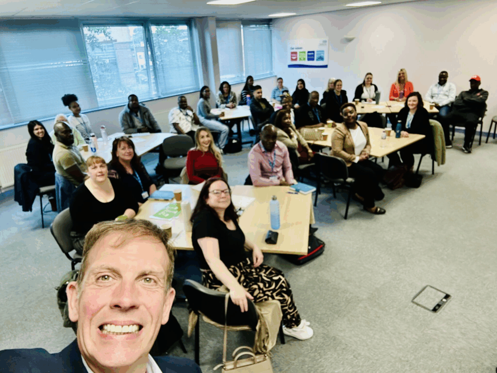 Selfie photograph by Anthony Hassell, Chief Executive of Pennine Care Foundation Trust. In the background new leaders and mangers at Pennine Care Foundation Trust are sat around a table for a group induction.