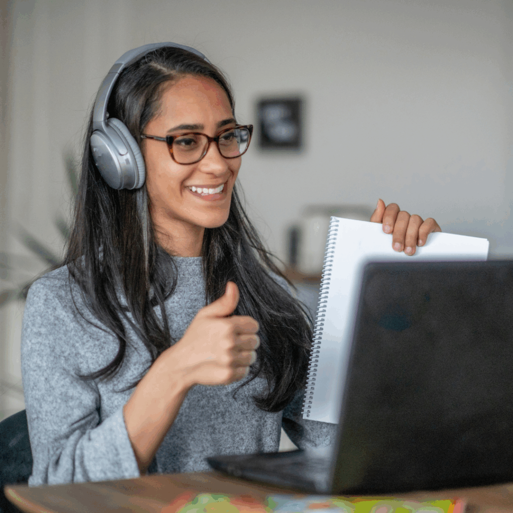 A smiling person wearing headphones in front of a laptop.